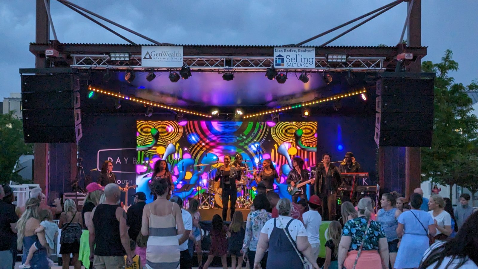 A full outdoor concert stage with line arrays and a gathered crowd