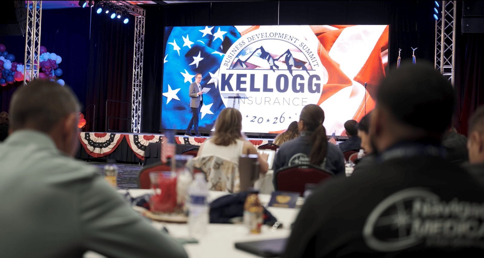 A keynote speaker in front of the branded Kellogg Insurance LED wall