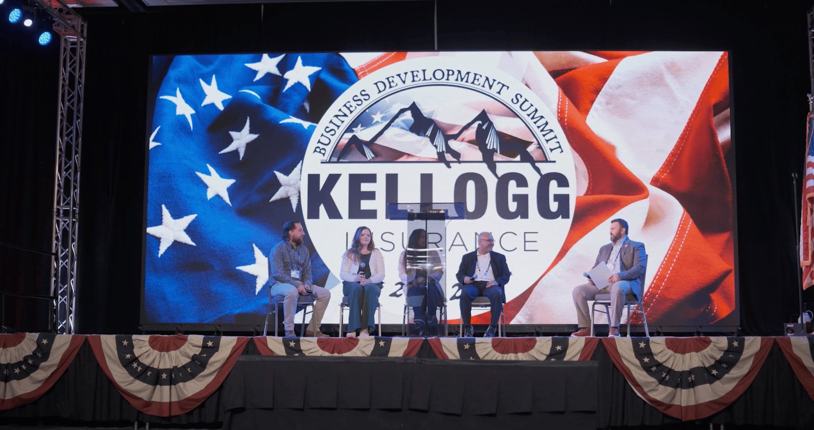 Panelists on stage framed by the Kellogg Insurance LED wall