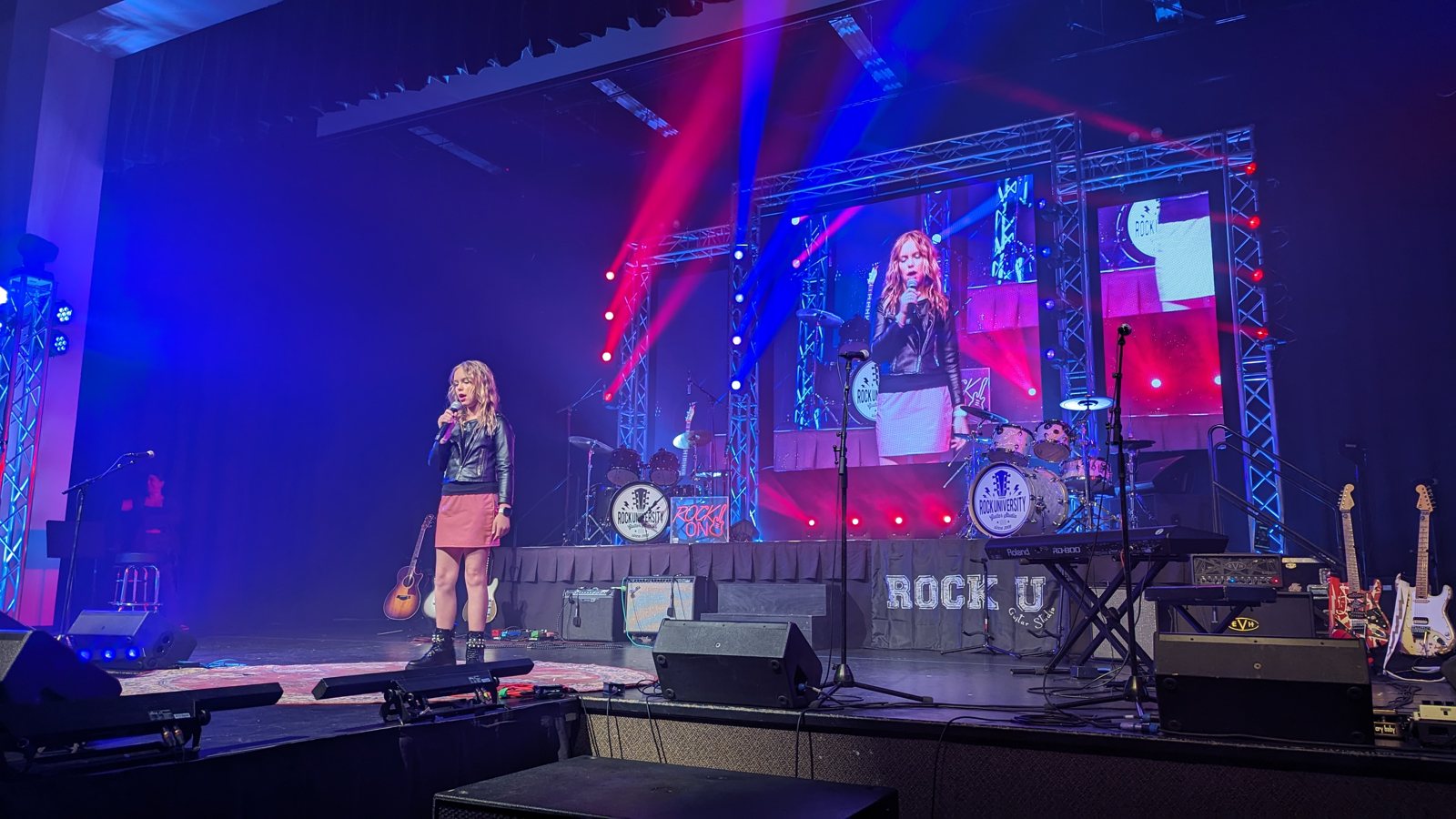 A young Rock University student singing on stage under full concert lighting