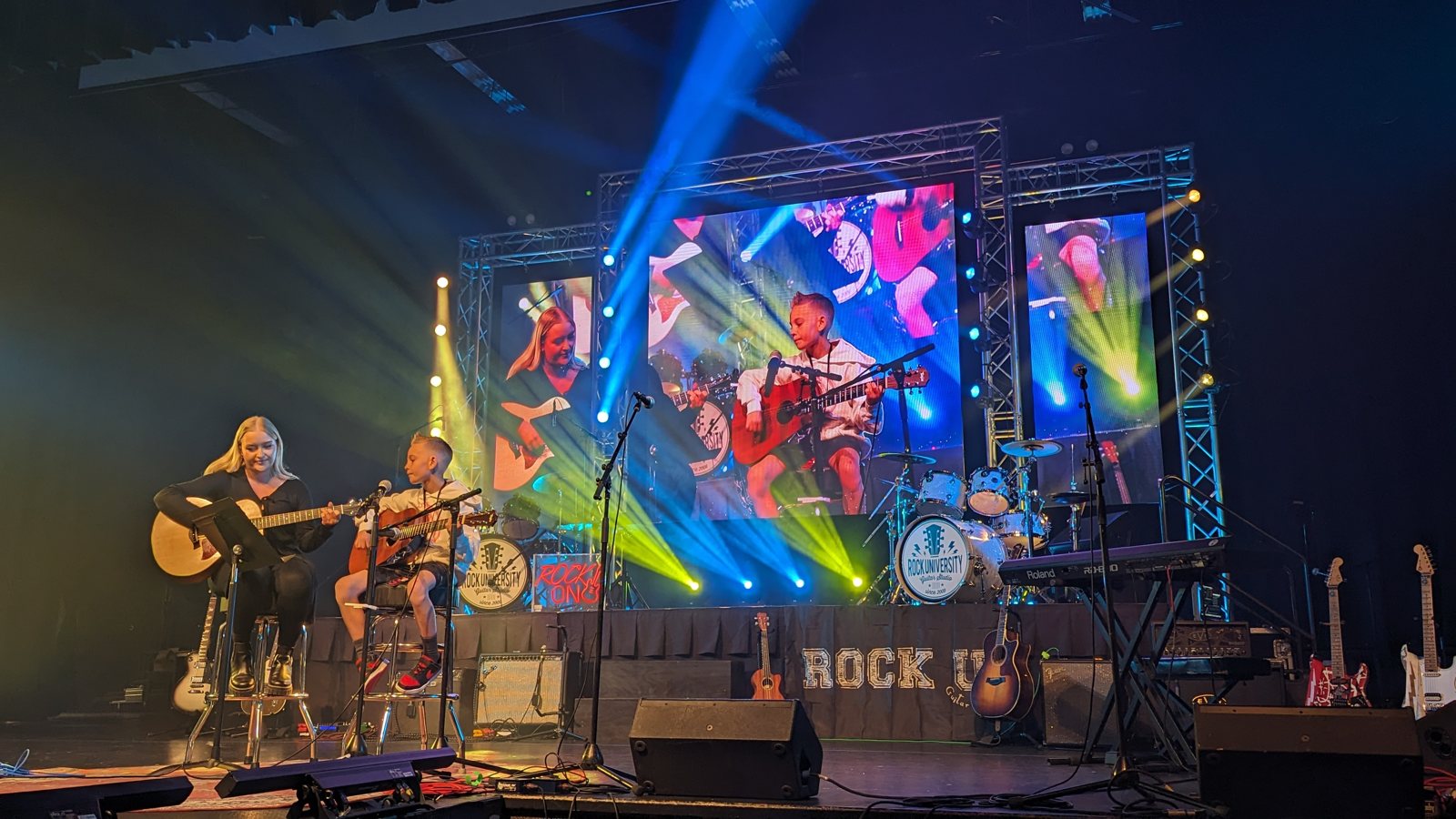 A student band under full concert lighting and haze on the Rock U Live stage