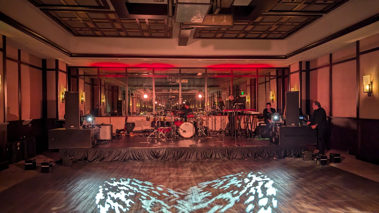 A live band set up in an elegant ballroom with red uplighting and a lit dance floor