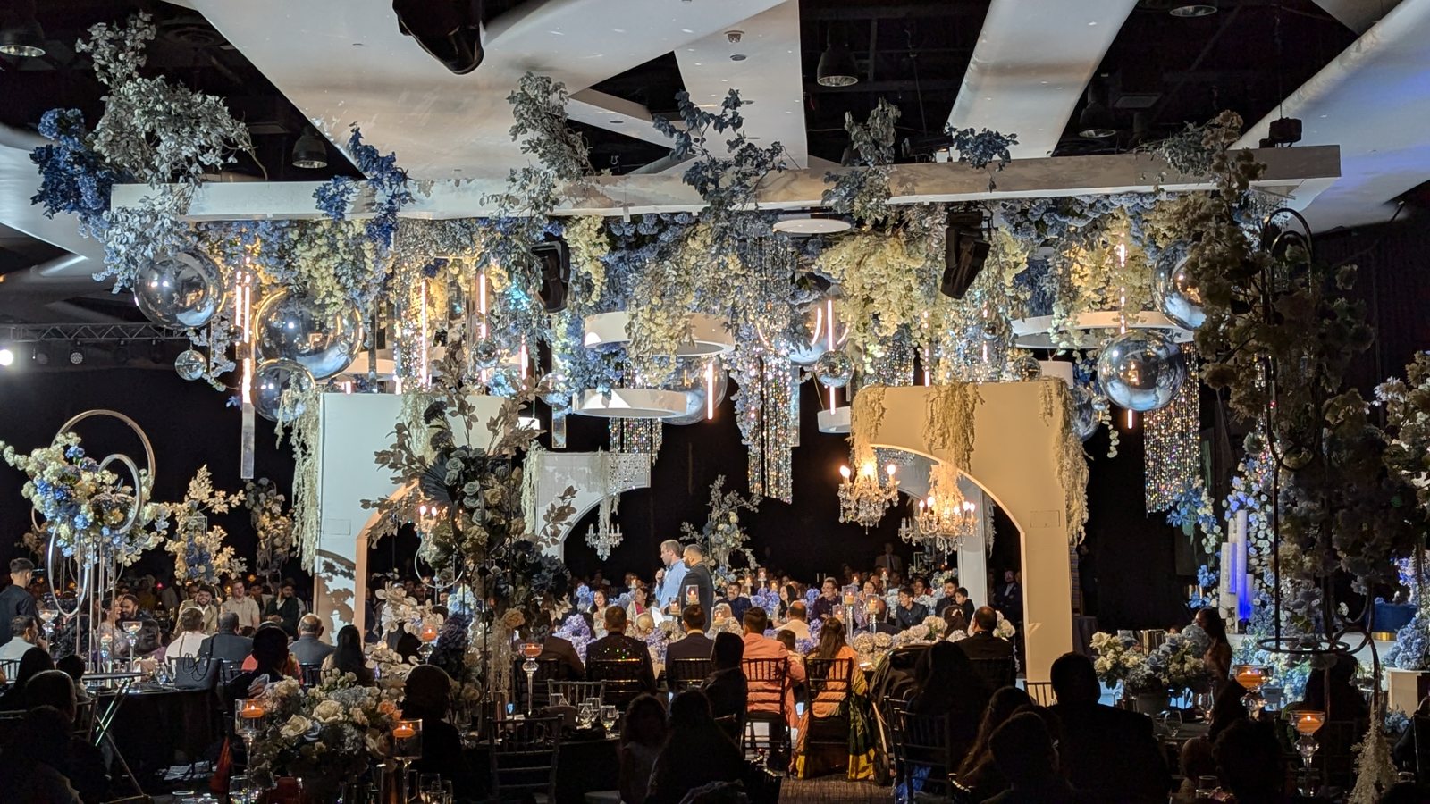A grand wedding ballroom transformed with blue and white floral and full production lighting